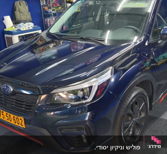 רכב כחול מבריק בחלל עבודה לדיטיילינג עם כלים ומוצרים ברקע